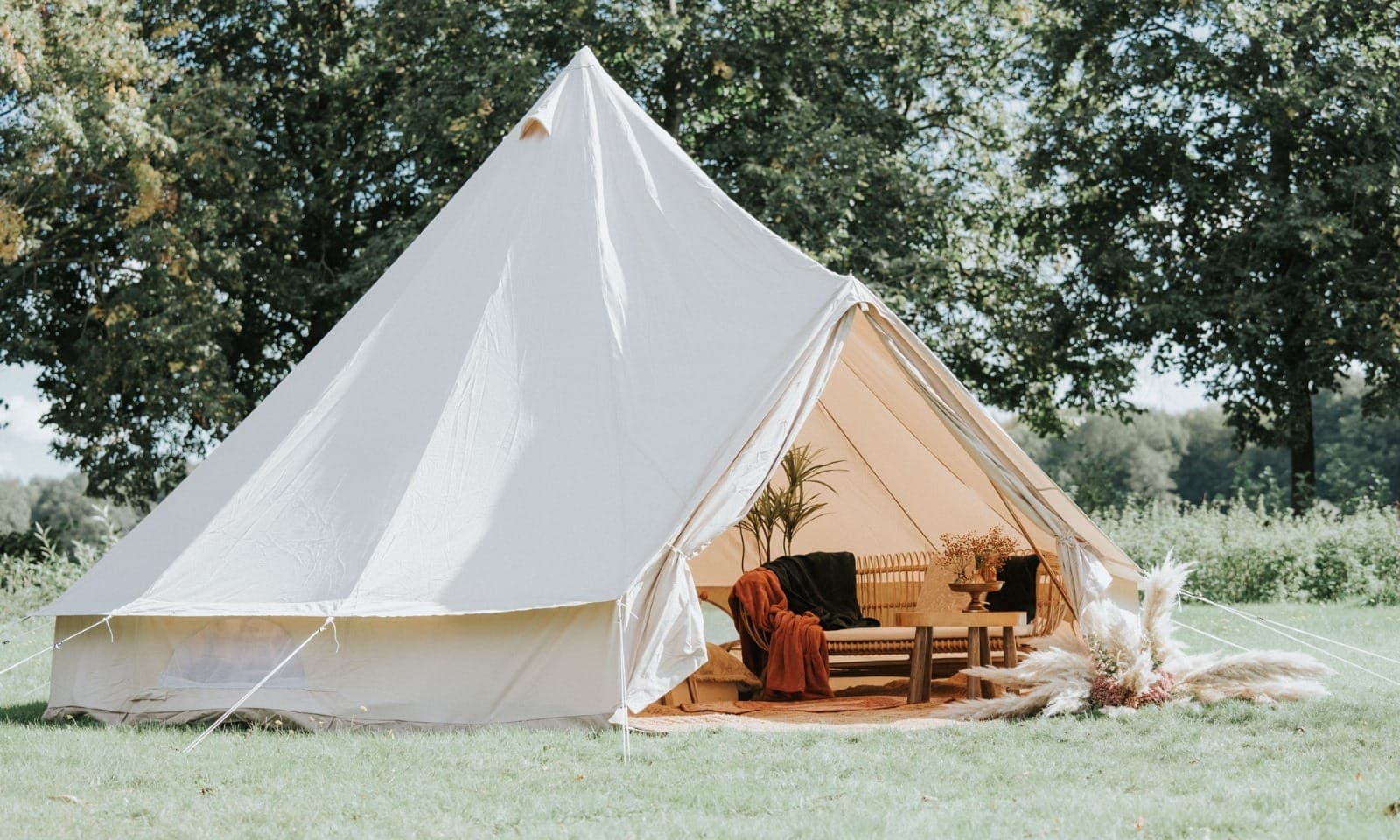 Belltent van Honeybell met de voorkant open: een bank met plaids, een tafeltje en pampasgras
