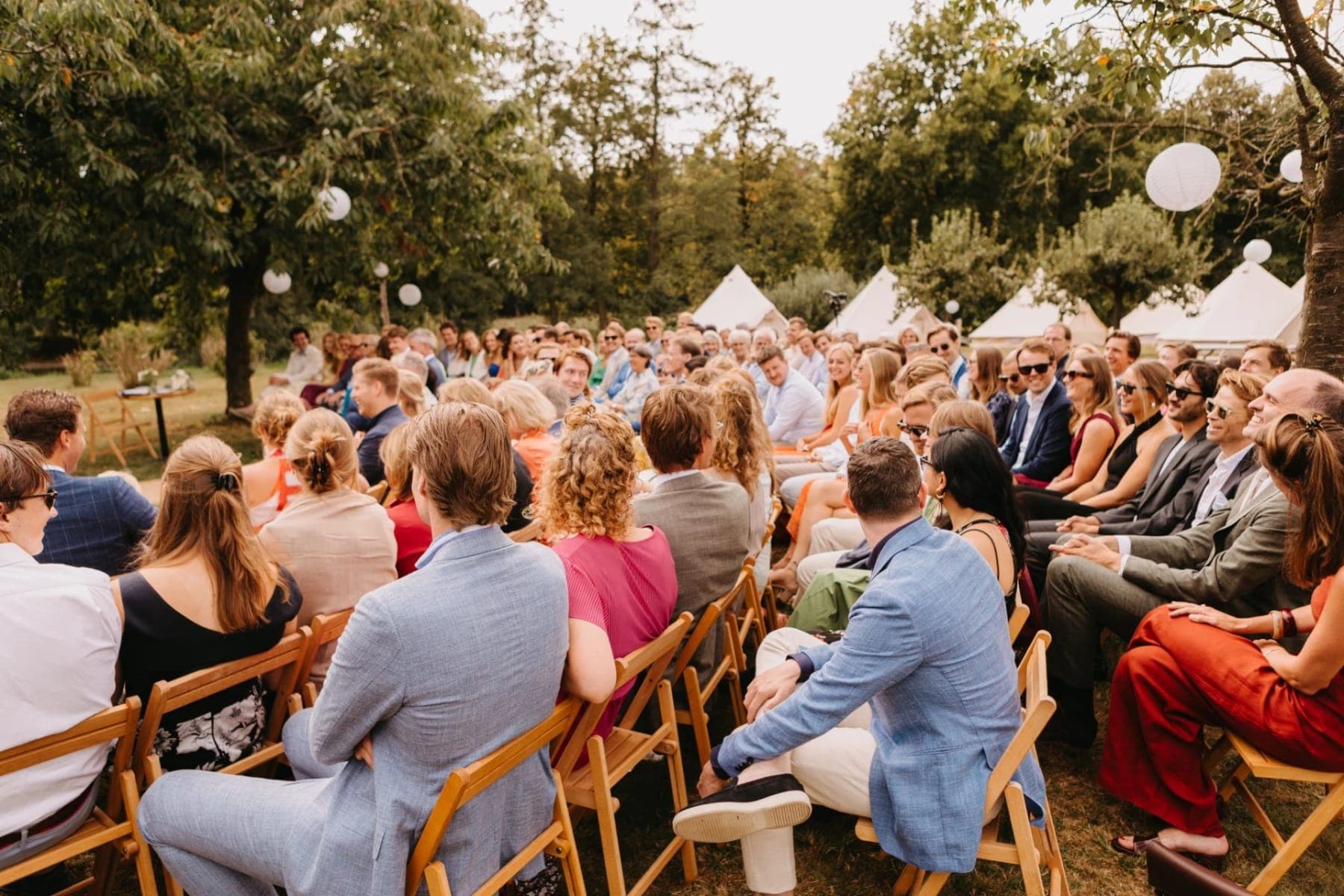 Gasten op houten stoelen tijdens de ceremonie, met de belltenten op de achtergrond
