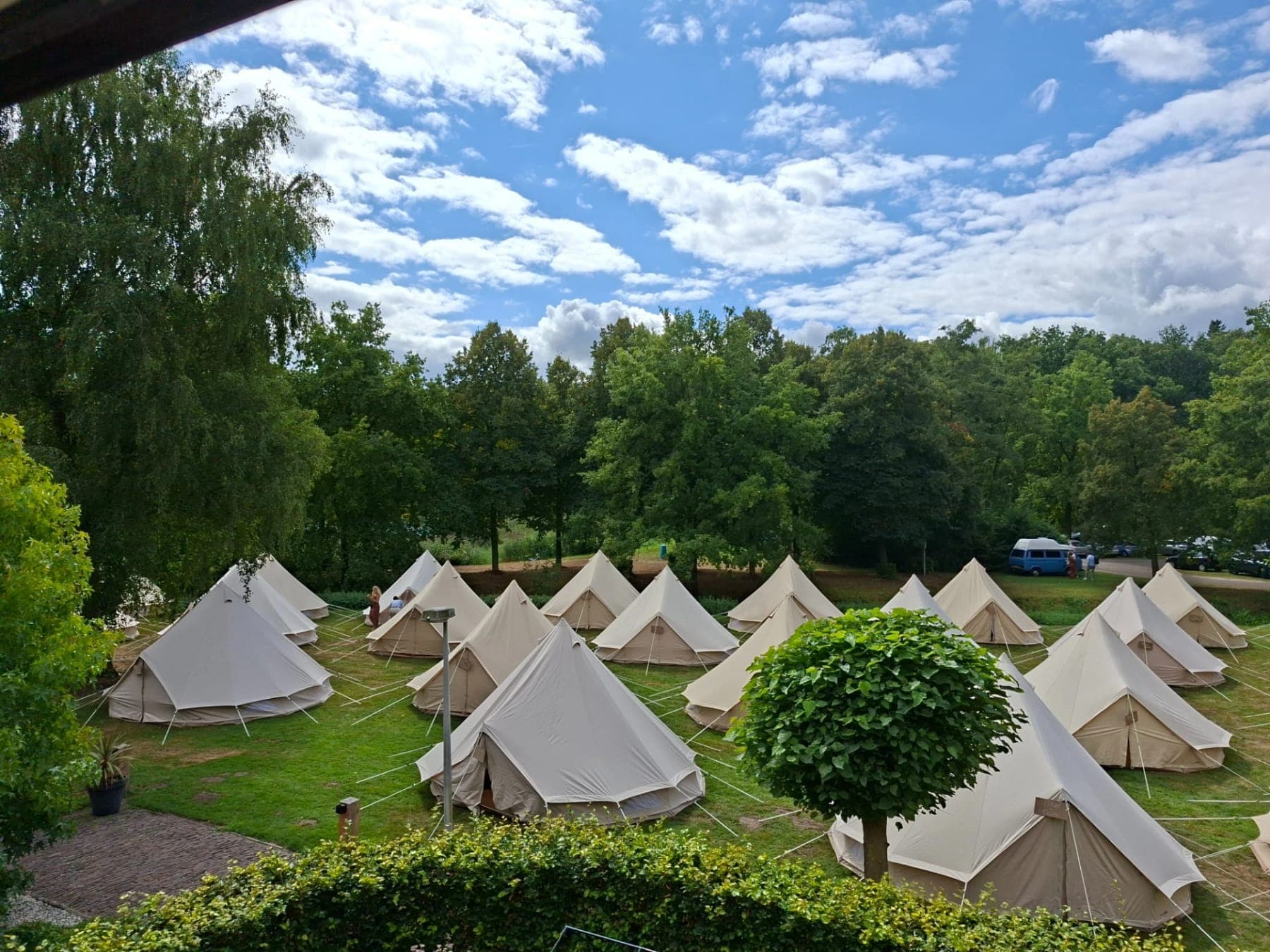 Een veld vol belltenten tussen de bomen, gezien vanaf een heuveltje