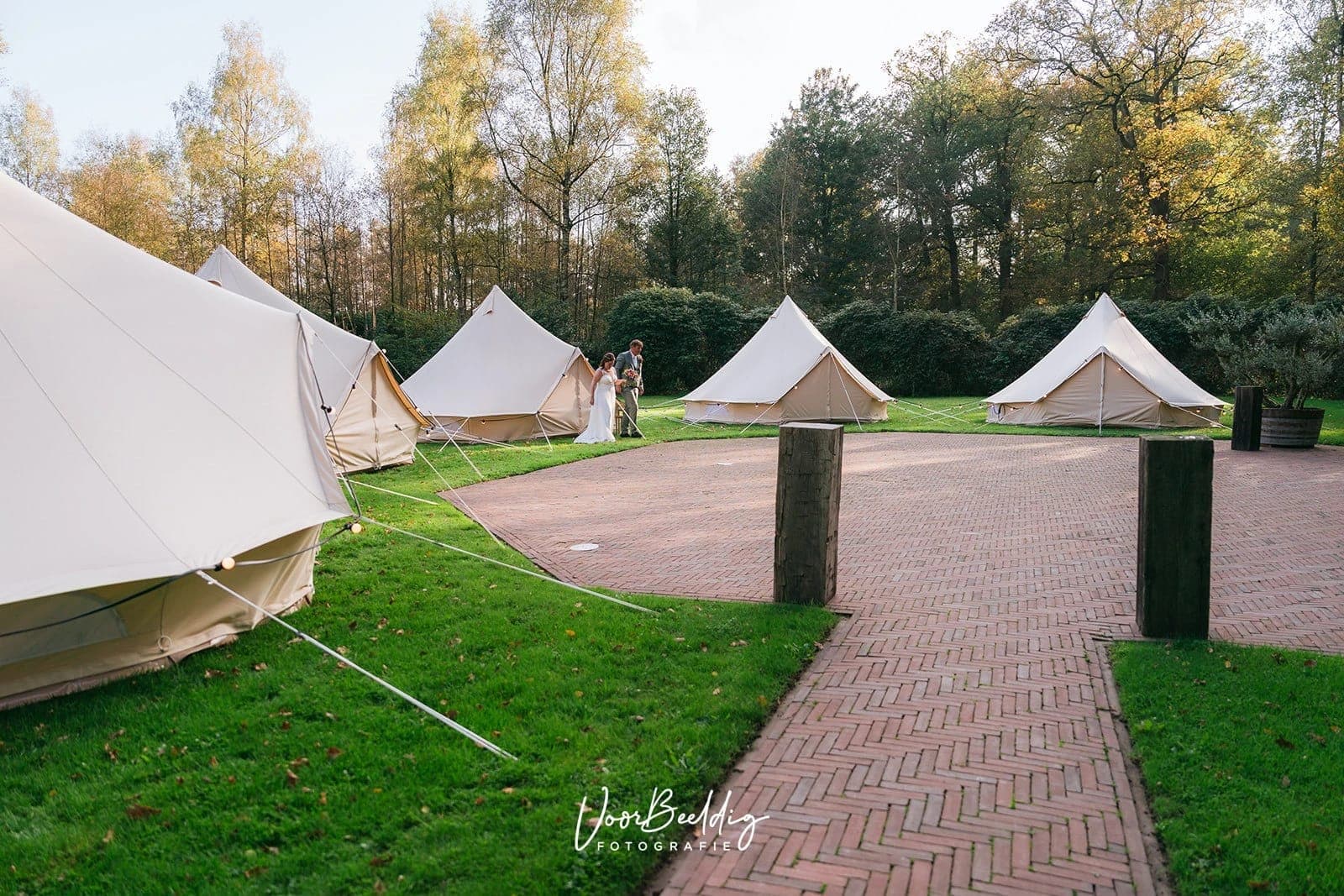 Belltenten rond een klinkerpad met een houten poort, op een landgoed